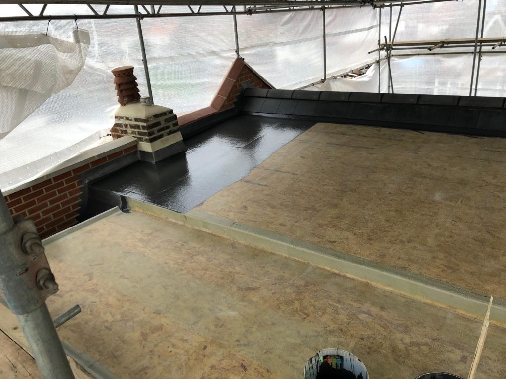 Flat roof waterproofing in progress with liquid membrane around chimney under scaffold protection